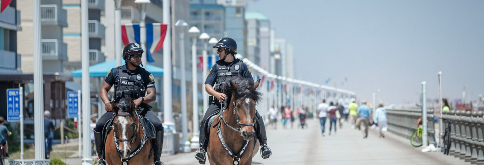 Two mounted patrol officers riding horses down boardwalk