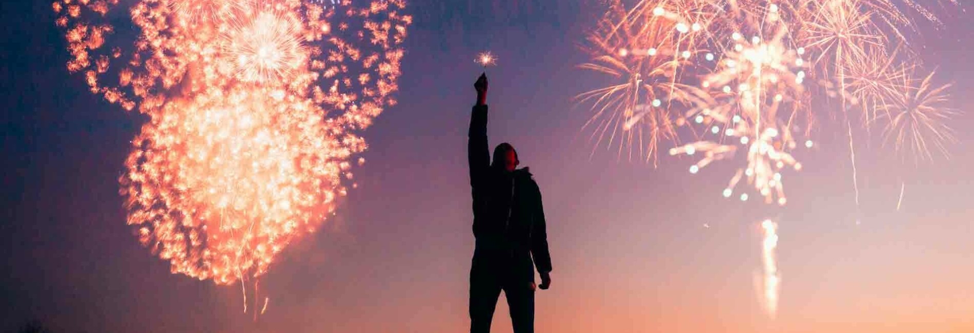 Man Holding Sparkler in Front of Fireworks