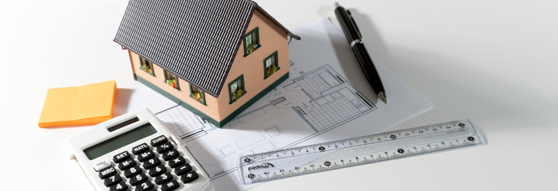 Calculator ruler pen and paper on table next to model house