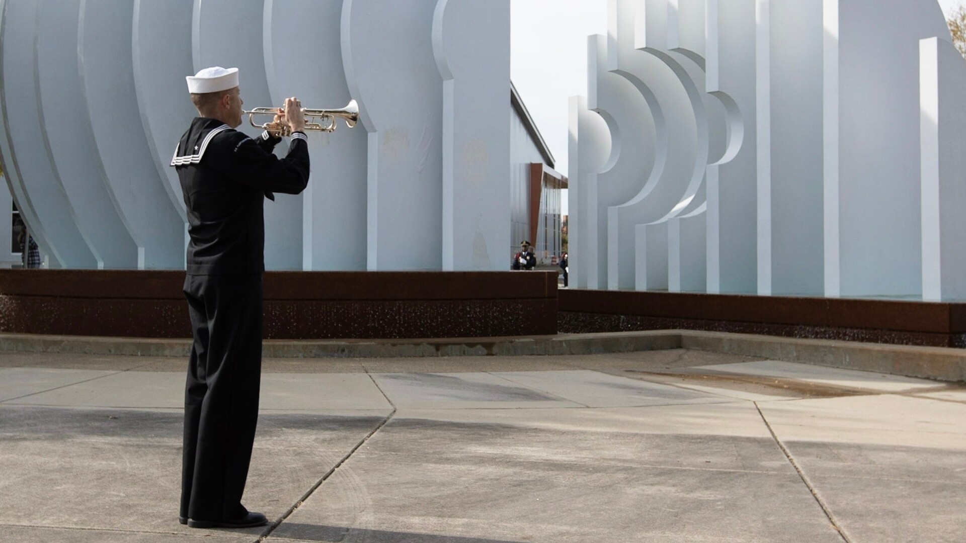 U S Navy enlisted member plays Taps on trumpet next to Tidewater Veterans Memorial