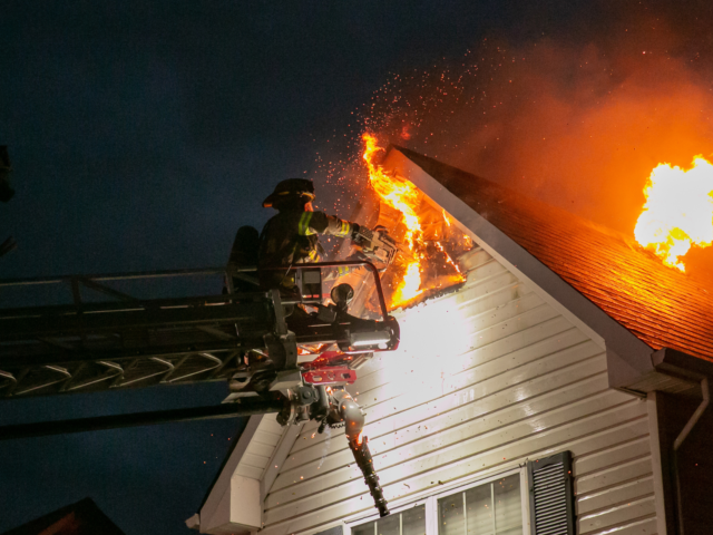 Firefighter on truck ladder hosing fire on house roof